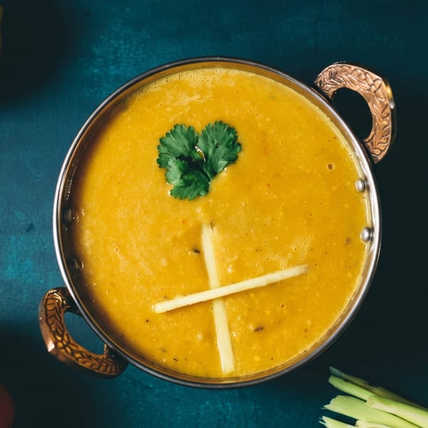 Golden yellow lentil dal in a brass bowl, garnished with cilantro and ginger strips.