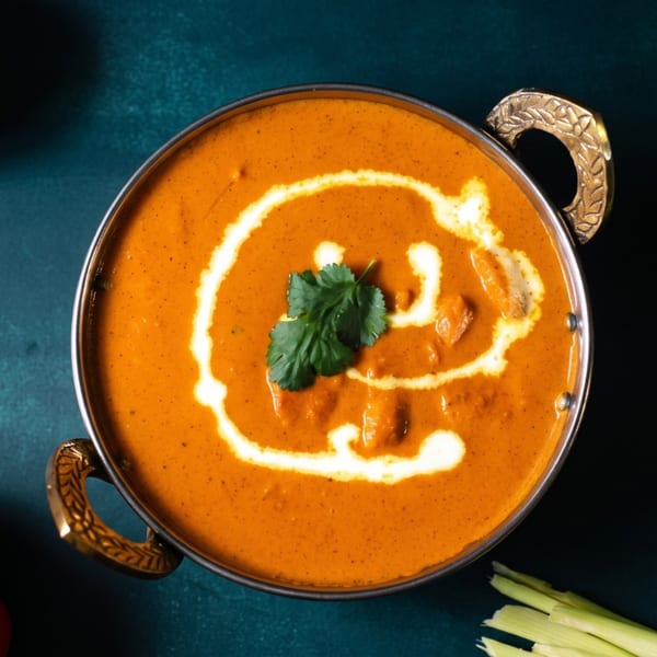 Overhead view of a copper bowl filled with orange curry, garnished with cream swirls and cilantro.