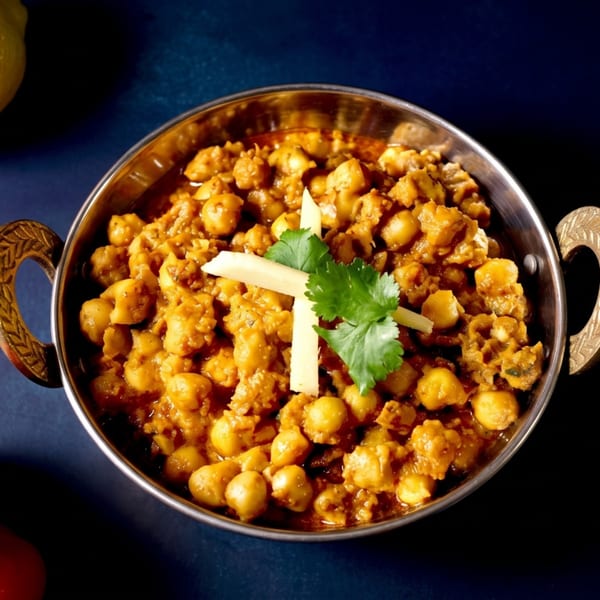 Chana Masala, a chickpea curry, in a copper bowl, garnished with ginger and cilantro.